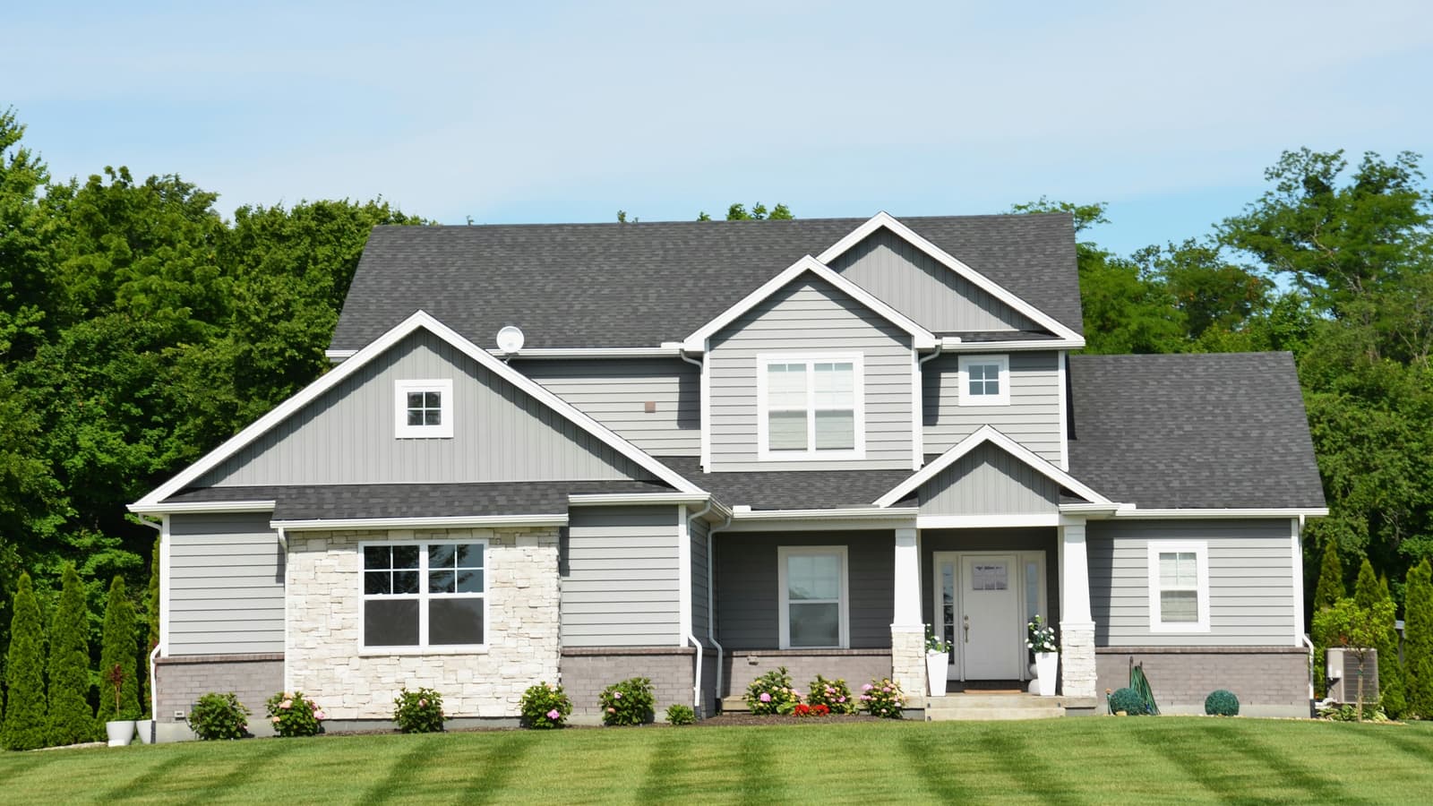 Two-story gray suburban house with stone accents and a freshly striped green lawn under a light sky
